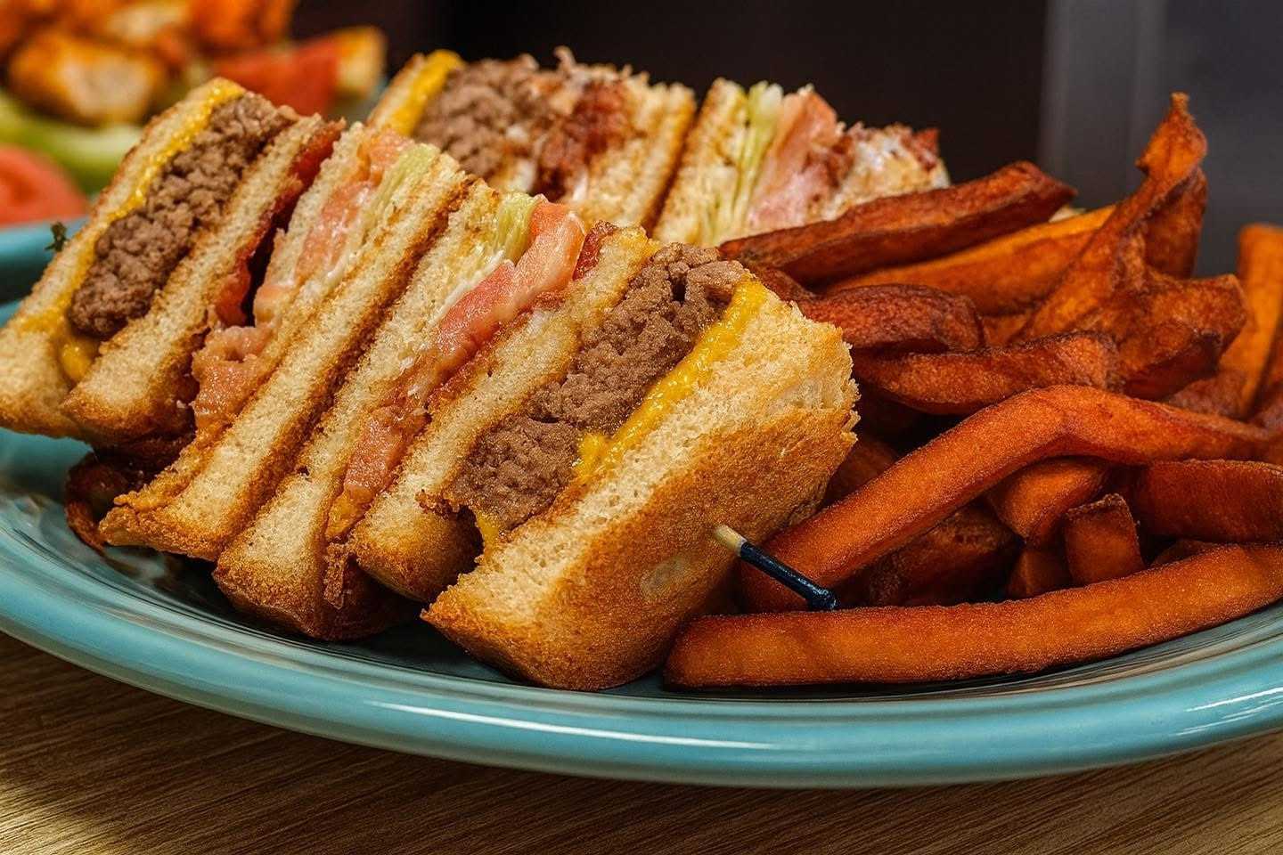 Burger sandwich with melted cheese and fries on a blue plate.