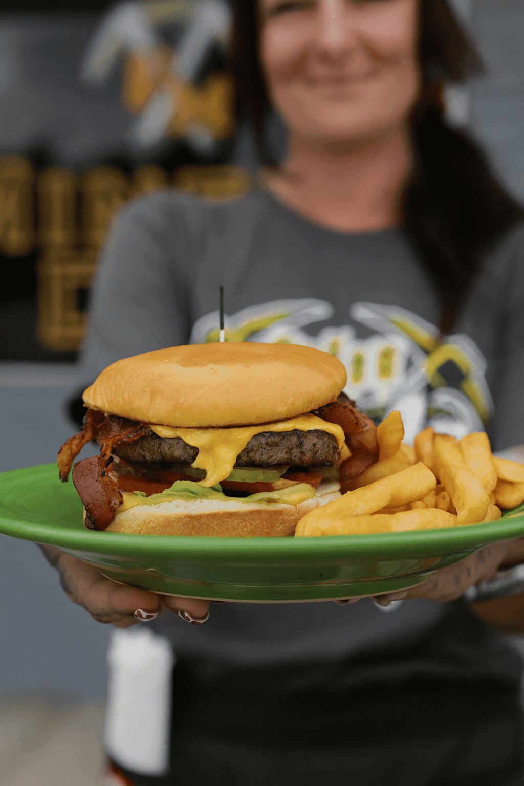 Burger with cheese and bacon, served with fries on a green plate, held by a person.